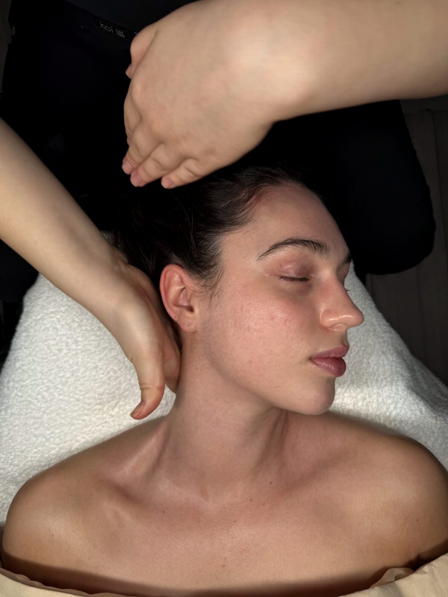 A serene client during a REGEN Clinic facial - the therapist's hands cradling the head and neck, natural skin in soft warm light.
